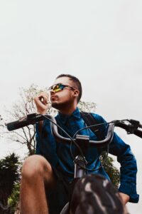 A young man with sunglasses poses confidently with his bicycle outdoors, embodying a sporty and trendy lifestyle.