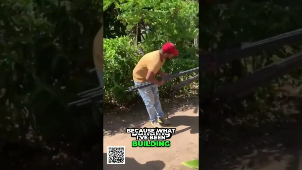 Man in a yellow shirt and red cap bends to carry metal pipes along a dirt path beside a railing, with a caption reading 'BECAUSE WHAT I'VE BEEN BUILDING' and a QR code nearby.
