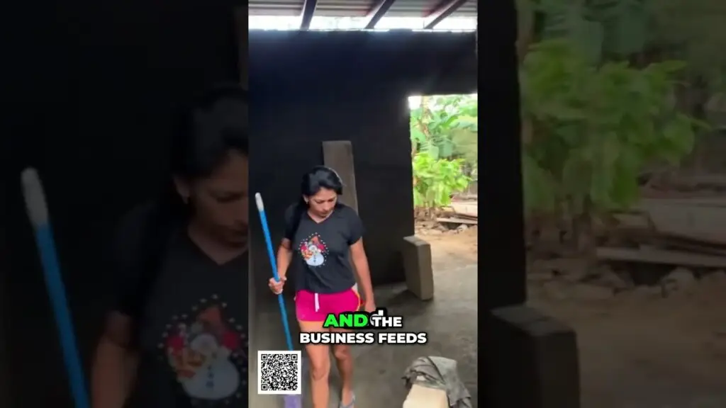 Woman in a black T‑shirt and bright pink shorts stands in a dark shed, holding a blue mop; a QR code and the caption “AND THE BUSINESS FEEDS” appear on the screen.