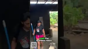 Woman in a black T‑shirt and bright pink shorts stands in a dark shed, holding a blue mop; a QR code and the caption “AND THE BUSINESS FEEDS” appear on the screen.