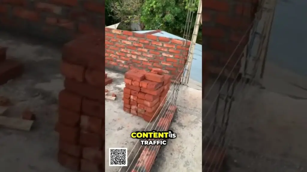 Content is Traffic Direct Your Audience for Income shorts - Travel With Glen Stack of red bricks at a construction site beside a partially built brick wall with vertical rebar and surrounding greenery in the background.