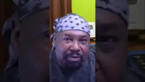 Close-up of a man wearing a star-pattern headscarf, looking at the camera in an indoor setting with a lime-green wall behind him.