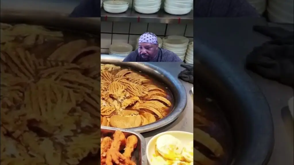 Amazing Pork Veggie Combo Must-Try Meal shorts - Travel With Glen Chef wearing a star-pattern bandana stands over a large frying pot filled with golden fried chips in a busy kitchen, with white bowls stacked in the background and trays of fried items nearby.