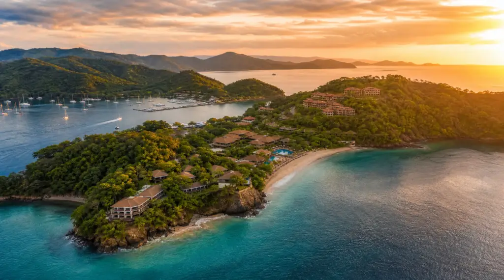 Aerial view of a tropical island resort at sunset, with turquoise bays, sandy beaches, and hillside villas covered in trees.