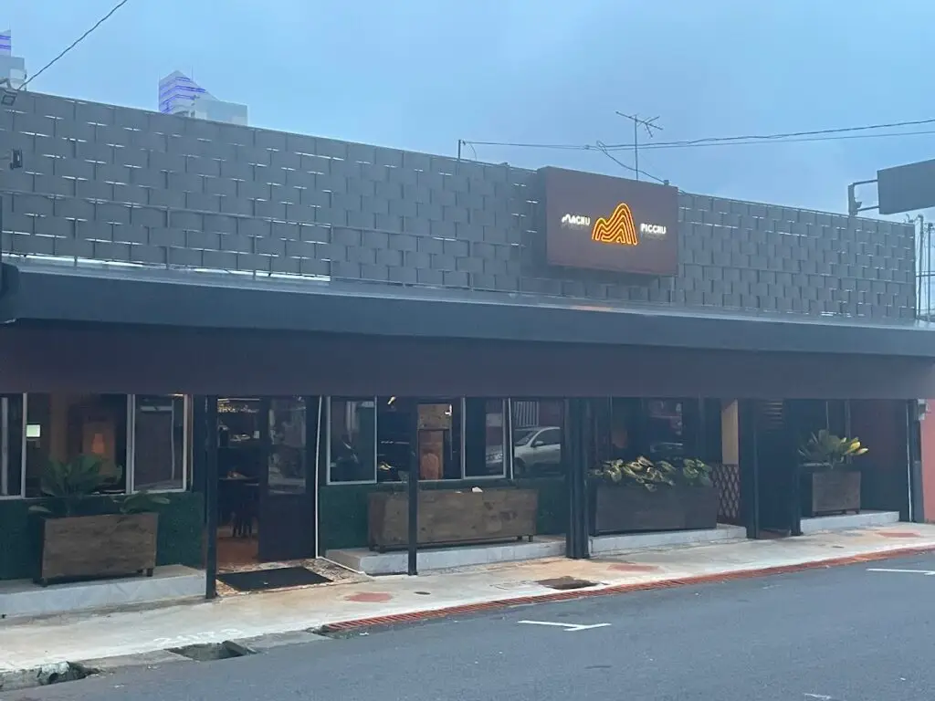Exterior of a modern storefront with large windows, planters, and a neon orange logo on a dark sign beside the entrance.